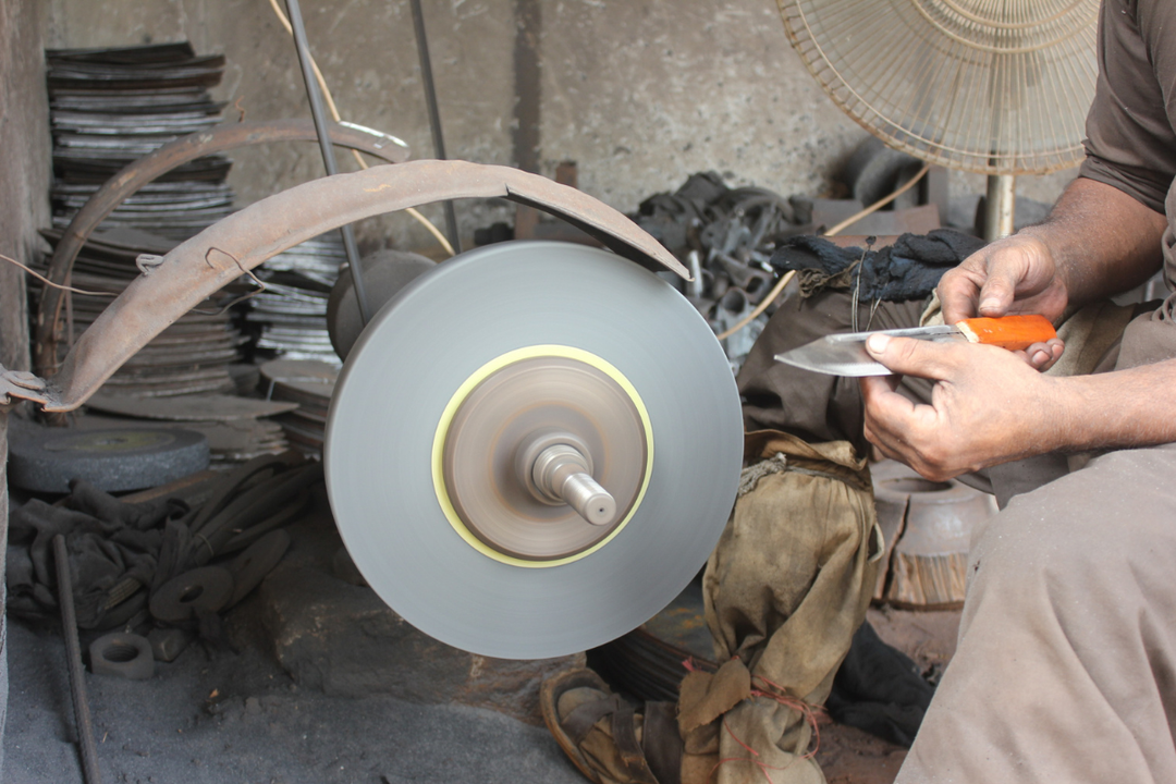 Beginner knife maker grinding steel blade bevel on workbench with angle grinder